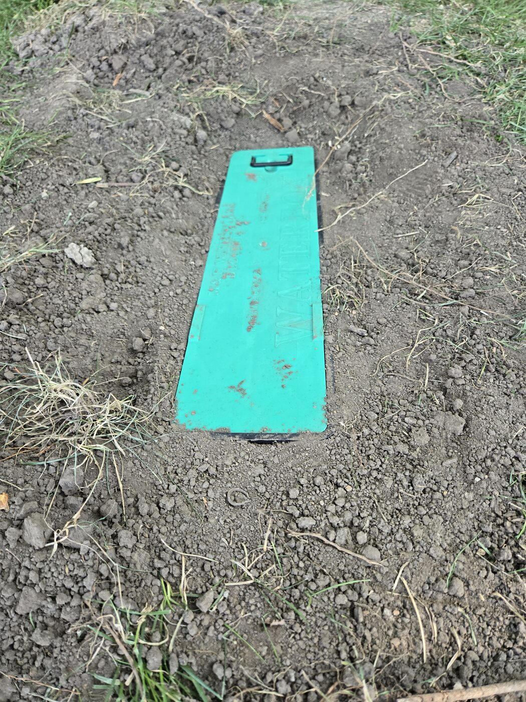Pop-up spigot water box closed and flush with the lawn — green lid marked WATER BOX, mower-safe and out of sight