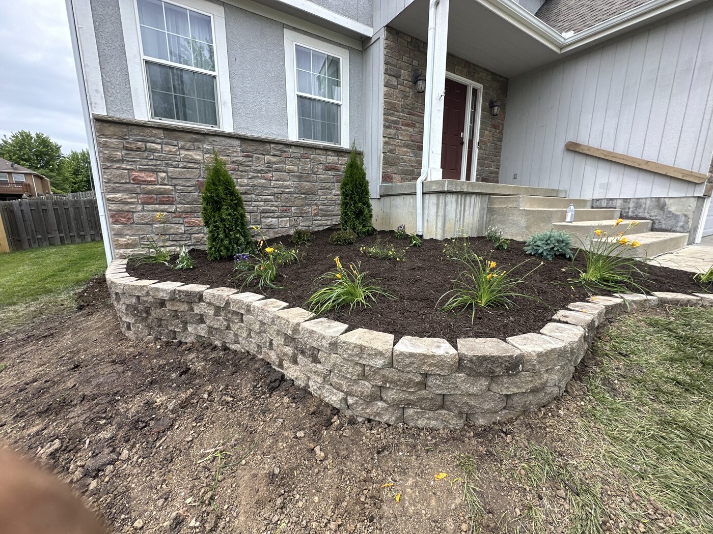 After: Attractive curved retaining wall with fresh mulch bed, flowers, small shrubs and evergreens next to the porch